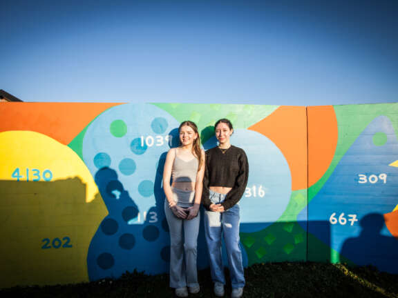 Two young people smiling as they stand in front of the newly completed mural that they had designed and created