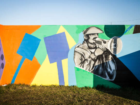 A section of a mural representing Dover's mining history. Painted in this section is a man wearing a flat cap, speaking into a megaphone, as well as multiple, colourful picket sign shapes.