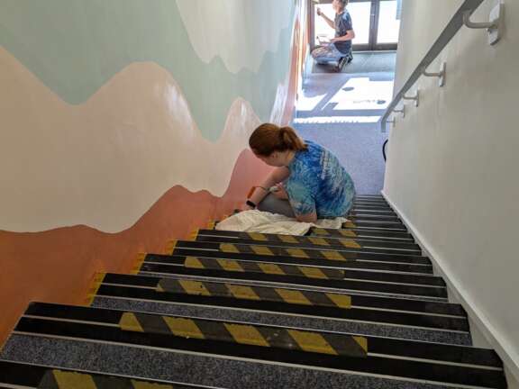 Young person painting pastel abstract mural down stairway