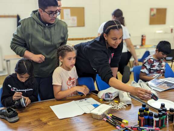 An artist and three young people choosing paints to decorate their trainers with