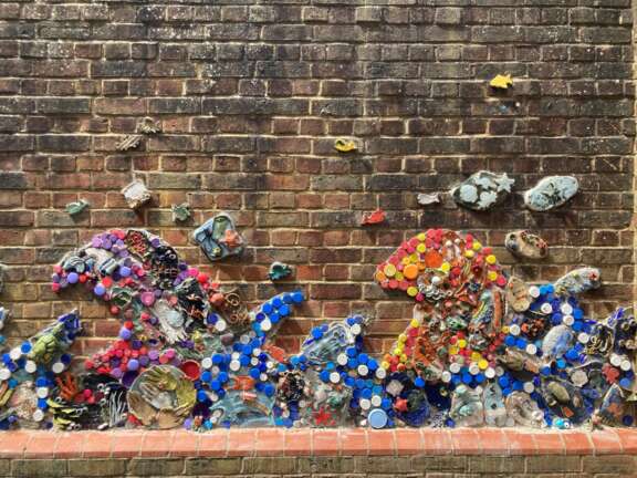 ceramic 3d mural on brick wall with plastic bottle caps in bright colours and different textural elements