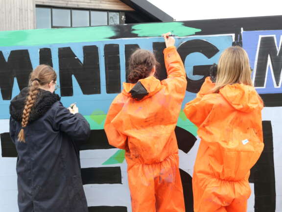 Three young people painting a mural designed to represent Dover's mining history with green and blue paint