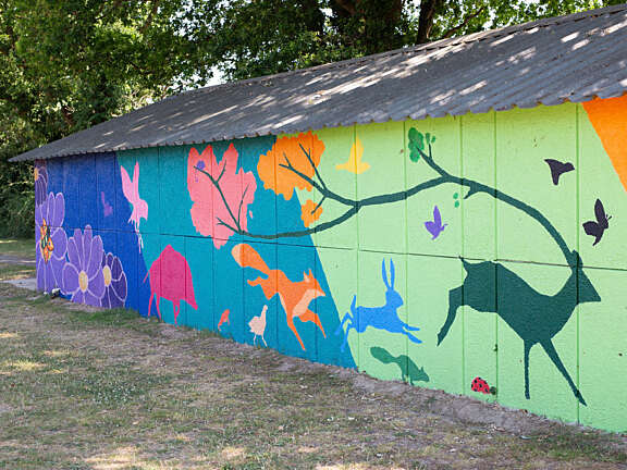 Close up of the colourful mural in greens, purples and blues. It features flowers, leaves and woodland animals.