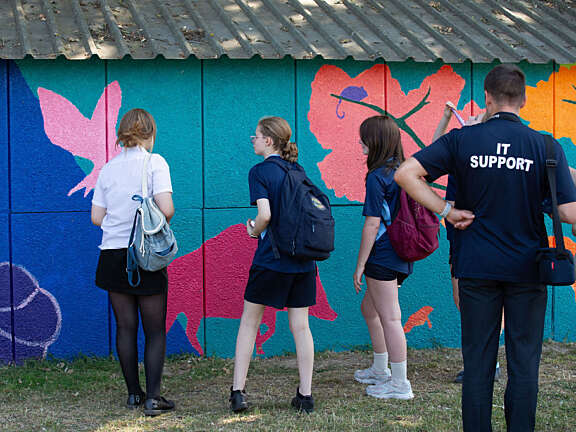 Five people stand looking close up at the mural with their backs to the camera.