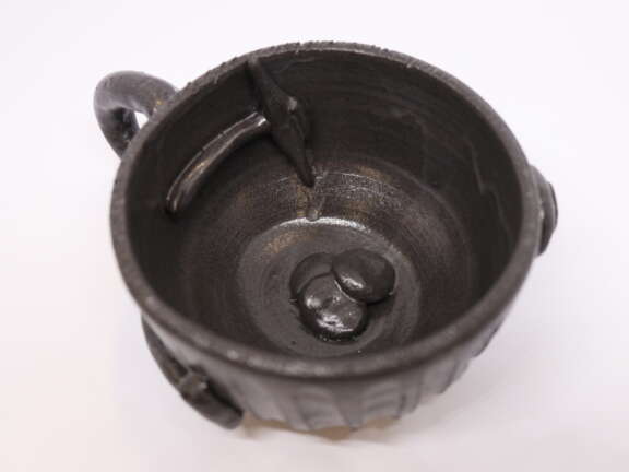 A handmade ceramic mug made using charcoal-based clay. It has a small ceramic pickaxe and rocks attached to the inside and bottom of the mug to represent Dover's mining history.