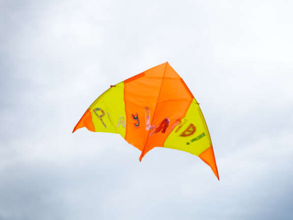 yellow and orange arrow-shaped kite with letters that read 'Playland!' flying in a grey cloudy sky
