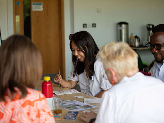 An Artswork staff member, Simi, is smiling with other members of the team as she works on a small painting