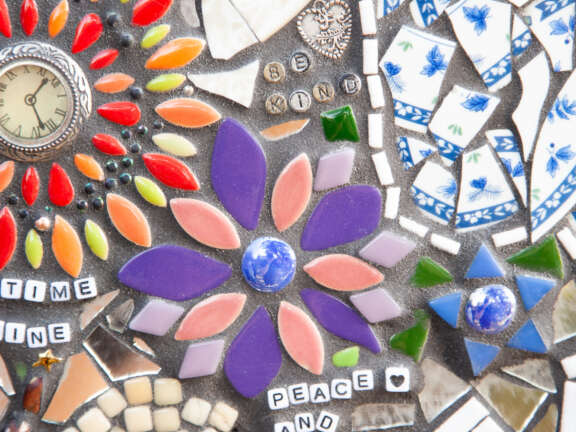 A close up of a mosaic designed by young people with letter beads embedded into it that say 'Be kind' and 'Peace and love'