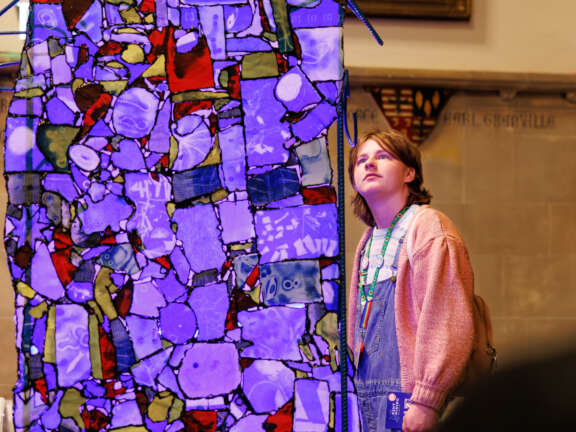 a young person looking at an artwork of coloured and patterned glass fixed together like a quilt and glowing