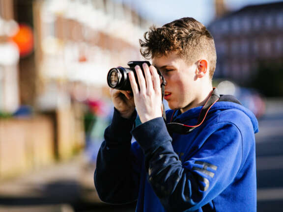 Young person looking through a DSLR camera lens to take a photograph