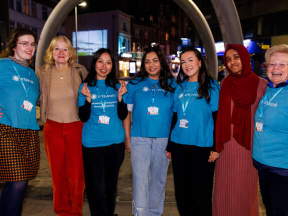 Seven Artswork staff wearing our branded T-shirts and smiling as they attend Dover at Night