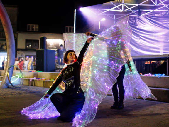 Two dancers performing in front of a stage waving light-up purple Isis wings
