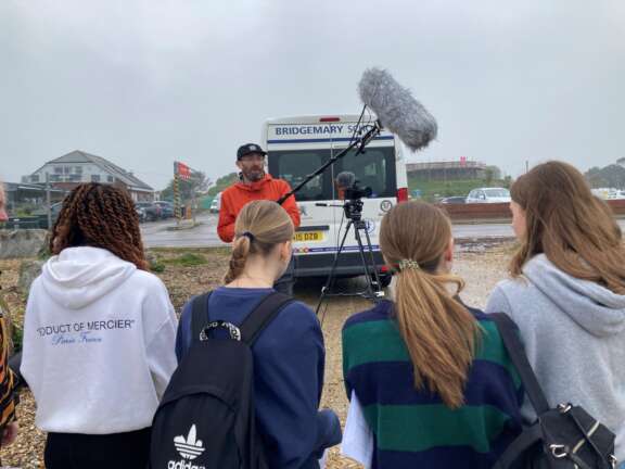 four young girls look away from the camera towards a man showing them filmmaking equipment