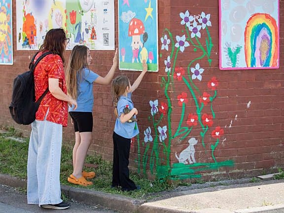 Two primary school age girls pointing at children's artwork on a brick wall, showing an adult that is with them