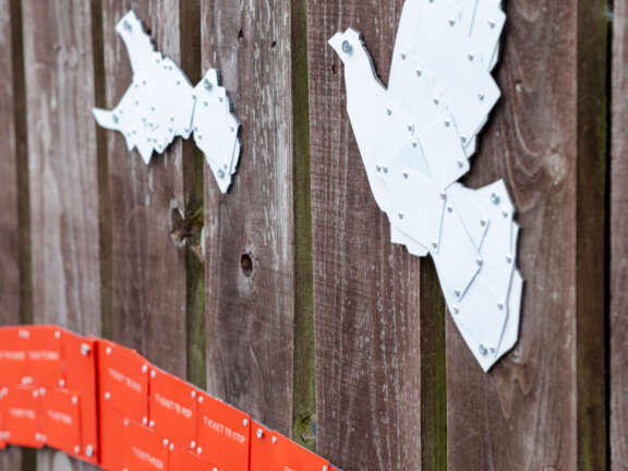 3d installation of white doves and orange and green lines made up of plastic train tickets