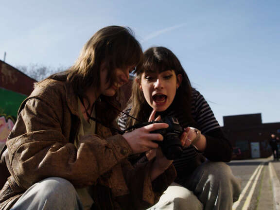 A young woman shows a mentor her photography on her camera. The mentor is enthusiastic about the work she's done.