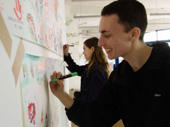 A young man and woman draw on paper that is stuck to a wall