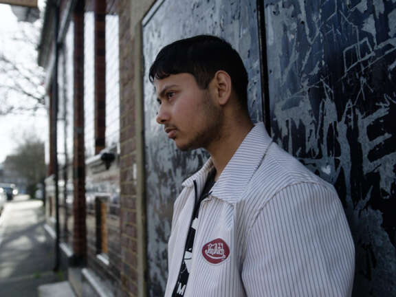 A young man leans on a doorway looking glum.