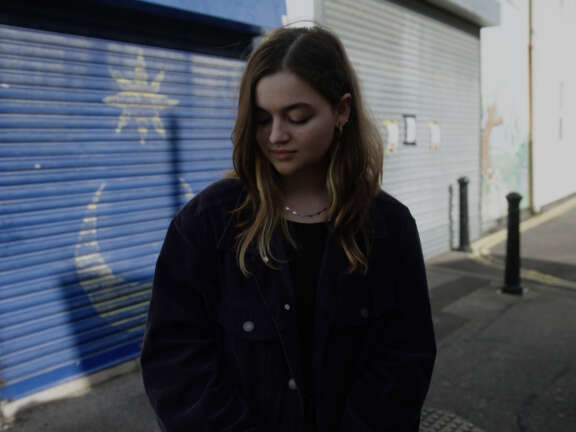 A young woman stands outside looking down at the ground. She looks sad and apprehensive.