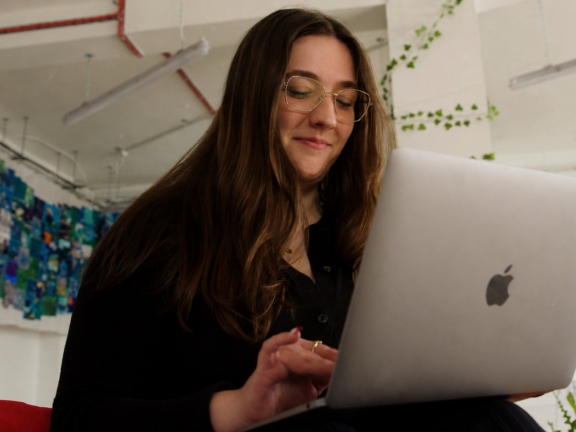 A young woman smiles as she looks at her laptop.