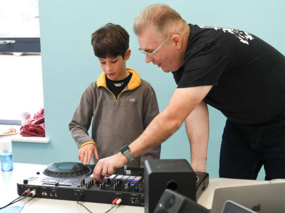 An adult teaching a young person how to mix music on a DJ mixing deck