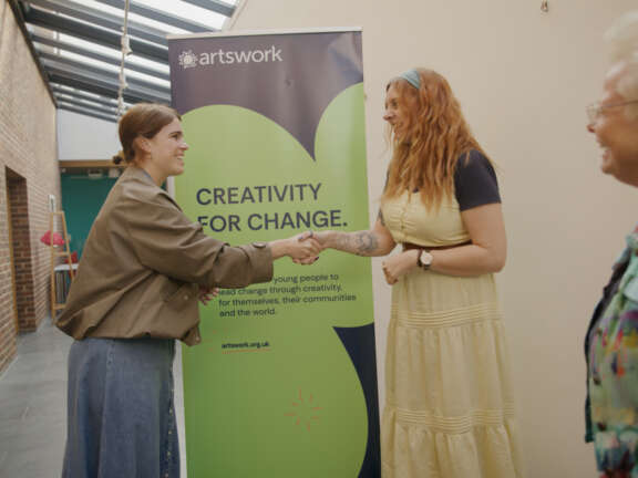 Princess Eugenie shakes hands with a young woman in front of the Artswork banner which reads 'Creativity for change'. Artswork CEO Louise Govier is visible in the right foreground.