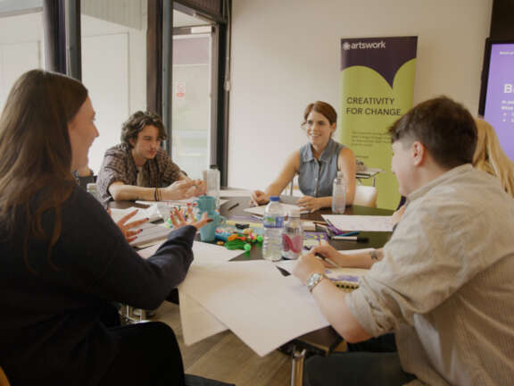 Princess Eugenie sits at a table with a small group of young people engaging in a group discussion activity.