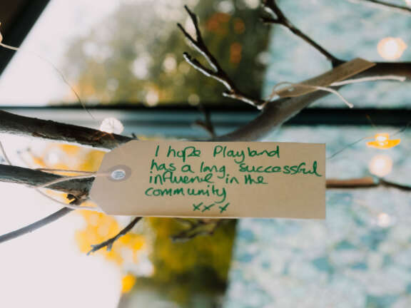 A tag hangs off a tree and says 'I hope Playland has a long and successful influence in the community.'