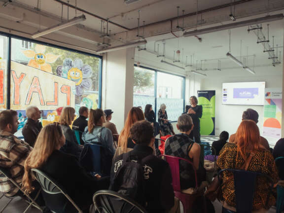 A group of people are sat down watching a presentation at the opening of Playland Creative Hub.