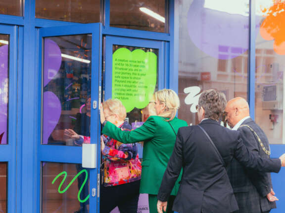 Four people walk through the front doors of Playland creative hub - there are patterns and logo's on the doors.