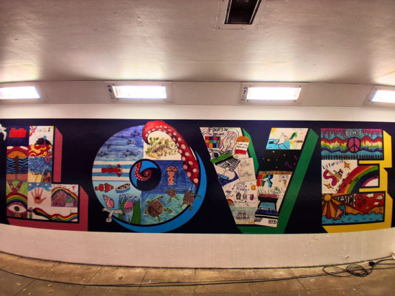 mural on wall of underpass - large letters that spell the word LOVE made up of lots of hand drawn images by children