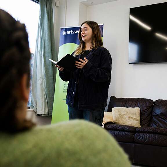 A young woman stands and reads poetry from a book