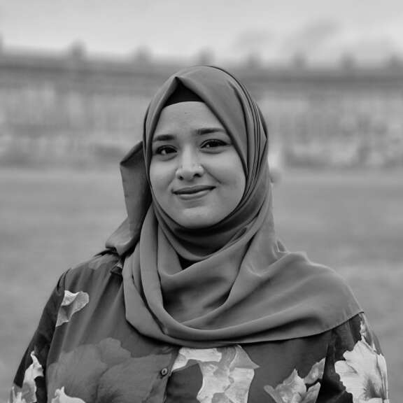 Afreen wears a hijab and floral dress and smiles at the camera