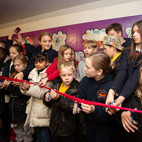 Group of school children all getting ready to cut a long ribbon with scissors
