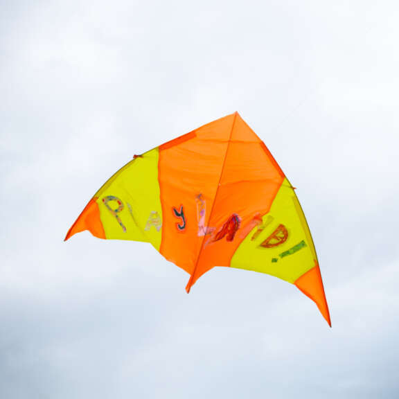yellow and orange arrow-shaped kite with letters that read 'Playland!' flying in a grey cloudy sky