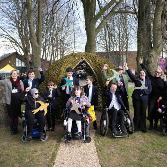 Diverse group of school children with physical disabilities celebrate in front of woven egg artwork holding ceramic swallows