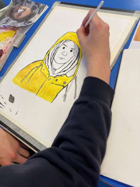 close up of someones hand painting a line drawing of greta thunburg in a yellow raincoat