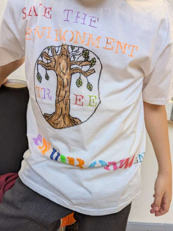 T-shirt decorated by child using pens that reads 'save the environment' with a drawing of a tree