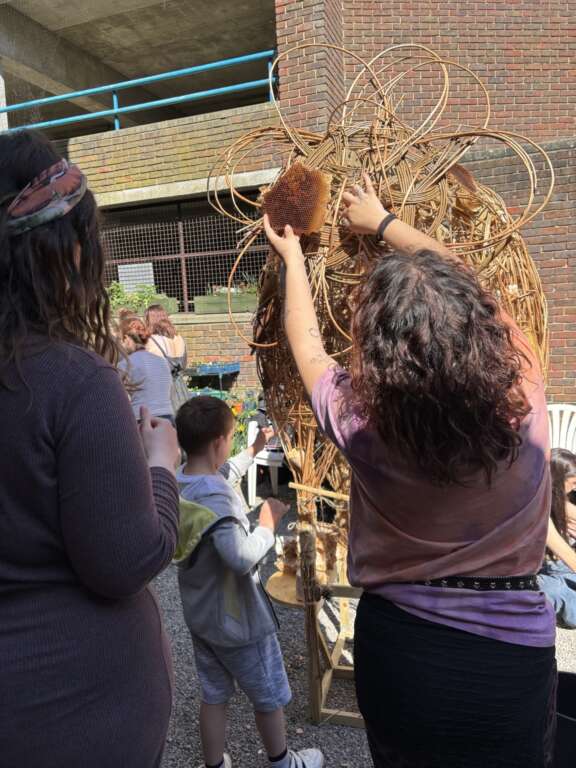 A young person fixing a piece of honeycomb onto a natural willow bio sculpture