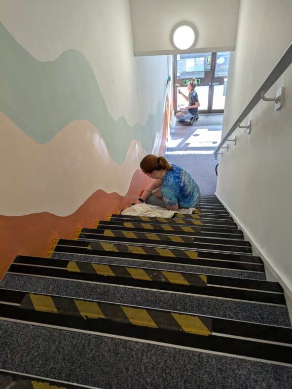 Young person painting pastel abstract mural down stairway