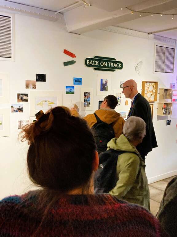 people observing an exhibition of work on a wall