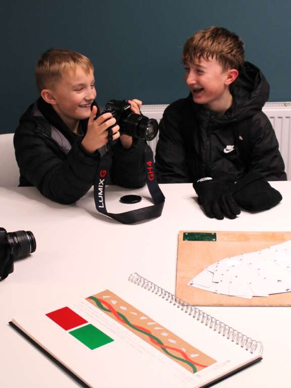 two boys looking at a camera sat in front of designs for 3D installation