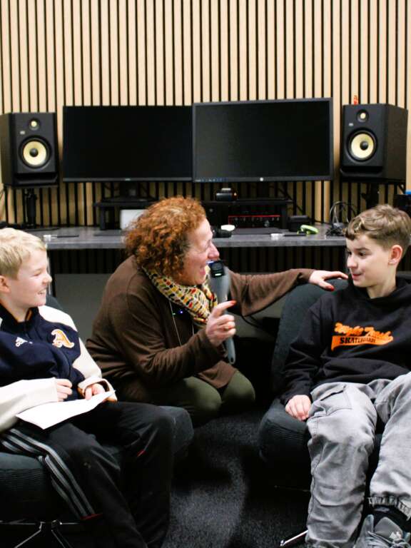 two young boys sat in a studio in discussion with a woman (Lucy Lomax) holding a microphone