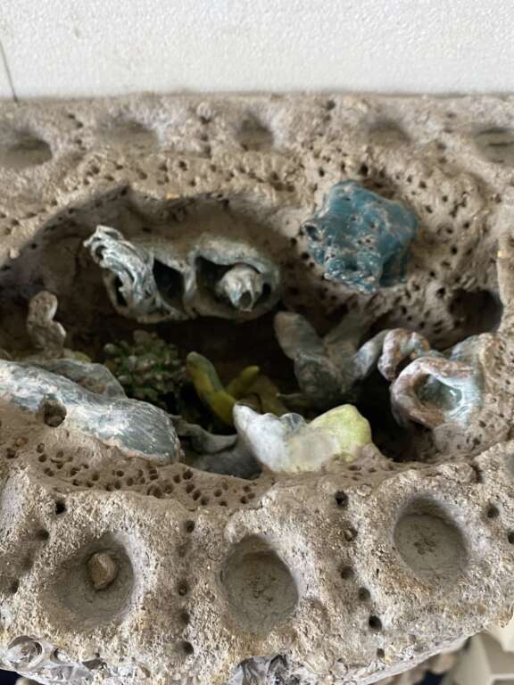 textured concrete semi circular basin-shaped artificial rockpool form attached to a vertical panel, inside the rock pools is an array of abstract ceramic forms in lots of varying shapes and textures in shade of blue and green