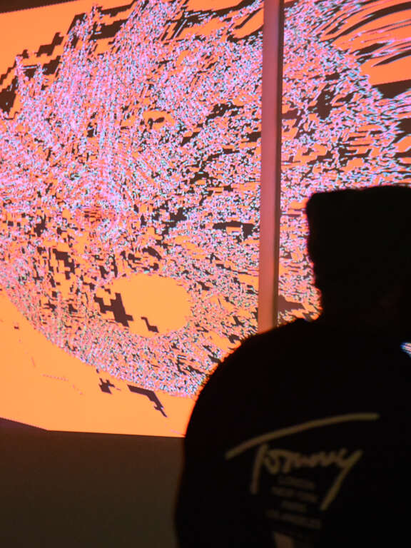 People in a dark room looking at colourful projections of pattern