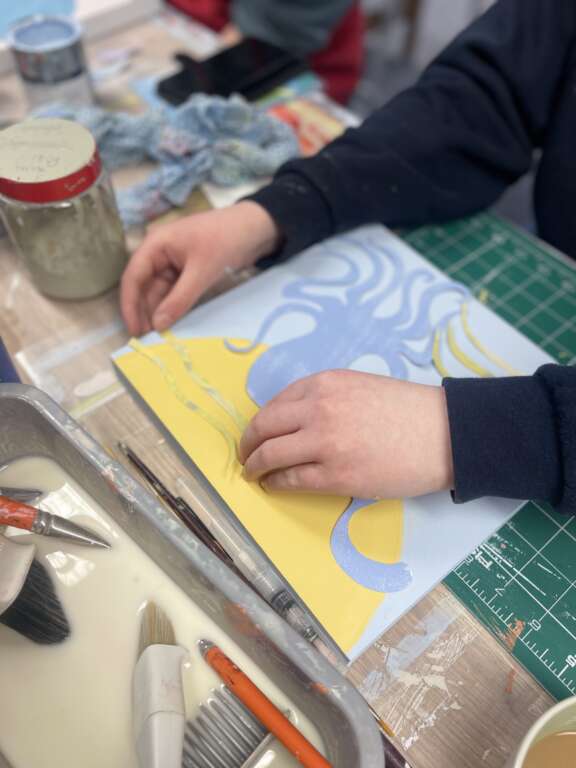 Young persons hands arranging paper on artwork of pastel blue and yellow octopus