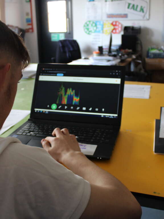 A young person using a laptop that shows colourful sound waves
