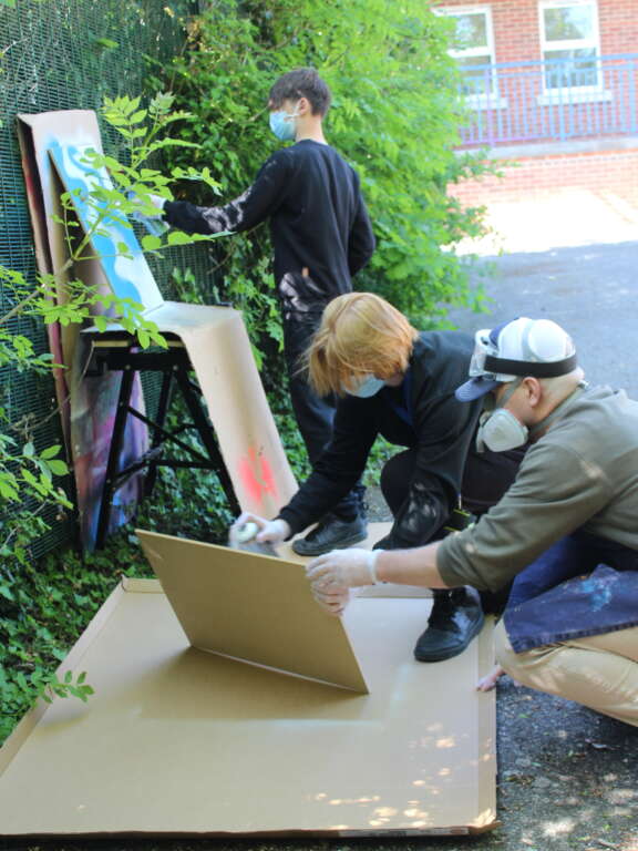 Young people wearing protective masks spray painting artwork outside