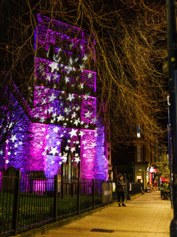 the front of a church lit up purple and pink with projections of hand drawn stars