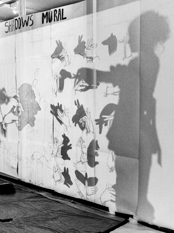 a mural depicting examples of hand shadow puppets with the shadow of a girl making her own hand puppet in front